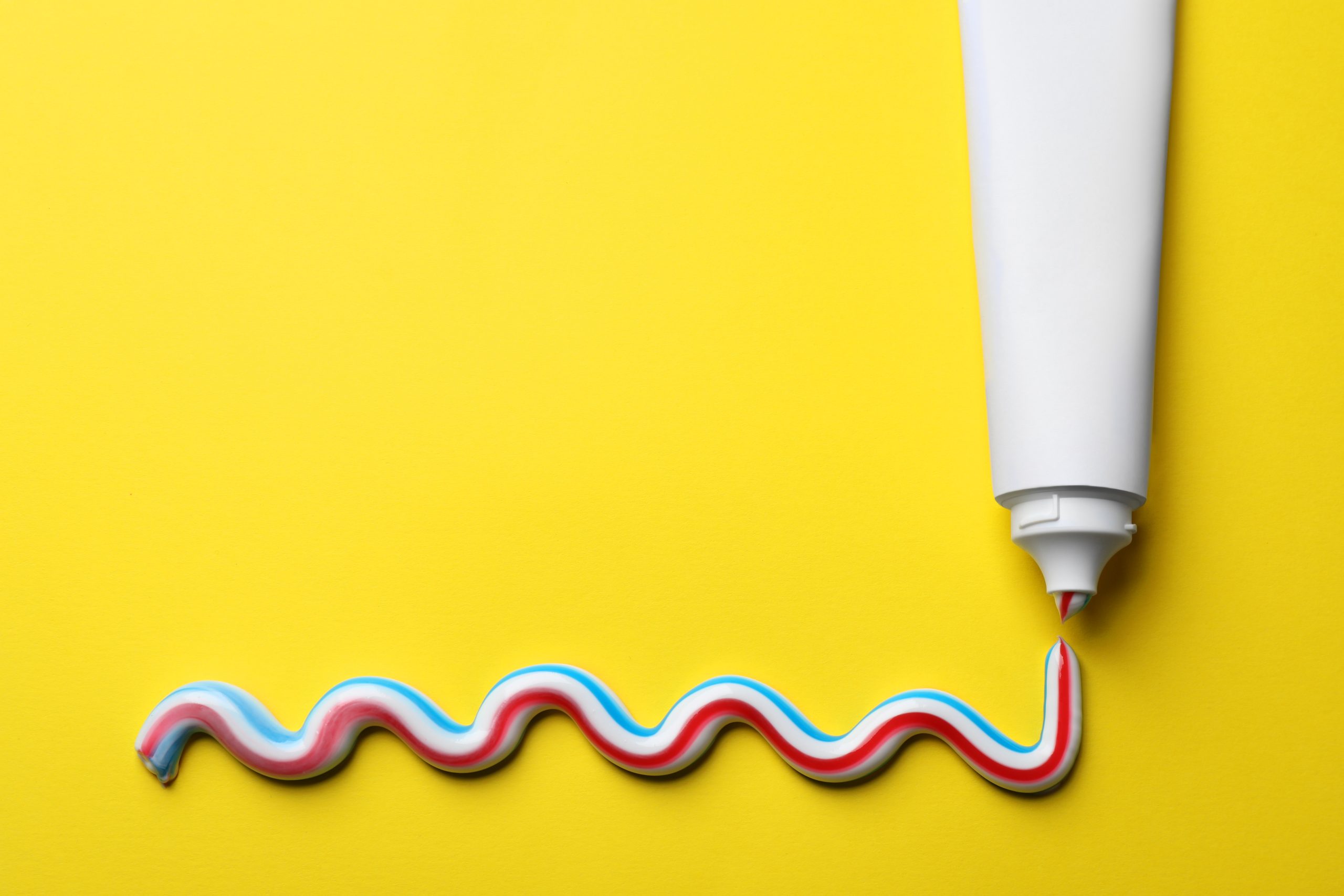 Blank tube with squeezed out toothpaste on yellow background, flat lay. Space for text