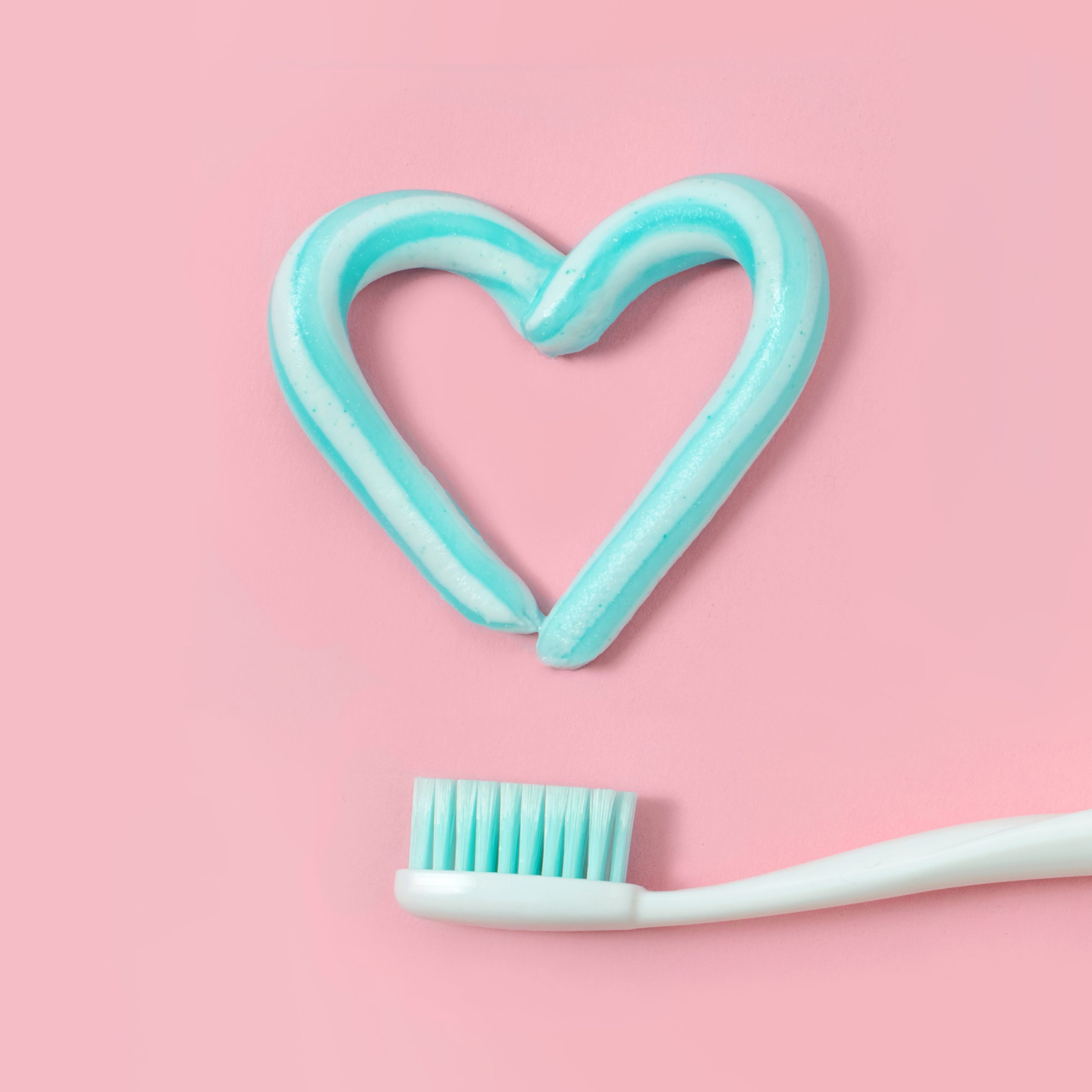 Toothbrushes and turquoise color toothpaste in shape of heart on pink background. Dental and healthcare concept.